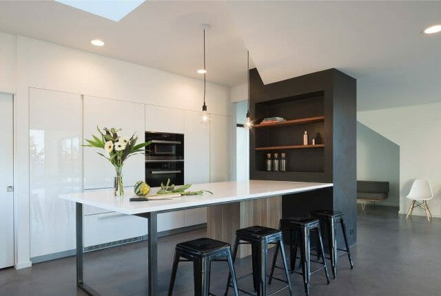 Minimalist white gloss kitchen with white quartz island, black metal bar stools and integrated appliances