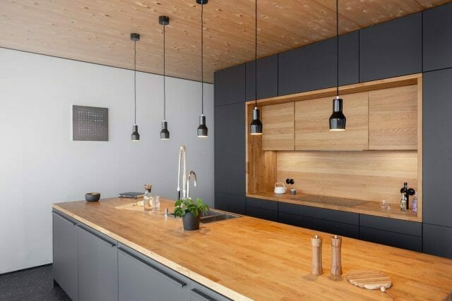 Matt black handleless kitchen with solid oak island worktop, open shelving and black pendant lights