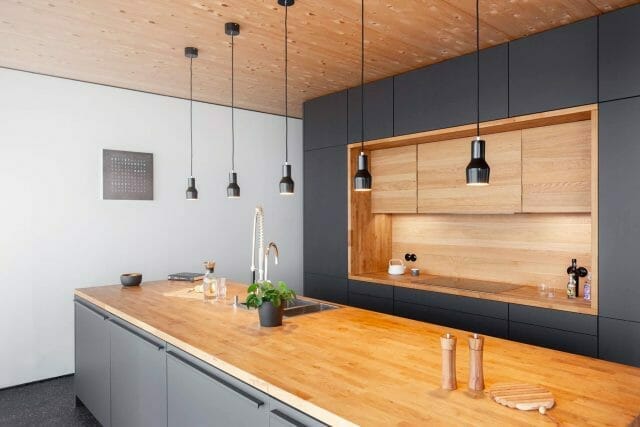 Solid wood breakfast bar worktop in a contemporary black handleless kitchen with open shelving