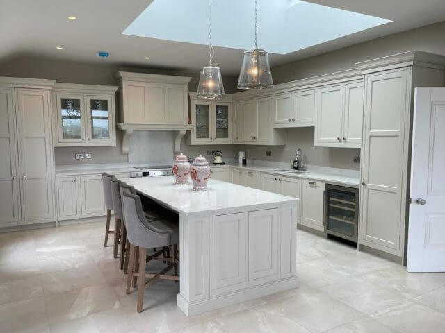 Classic cream in-frame kitchen with white quartz island, velvet bar stools and glass pendant lights under a roof lantern