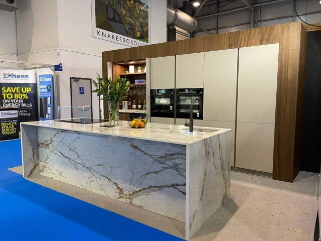 Tolle Kitchens handleless kitchen display at the Homebuilding and Renovating Show featuring a statement marble-effect waterfall island