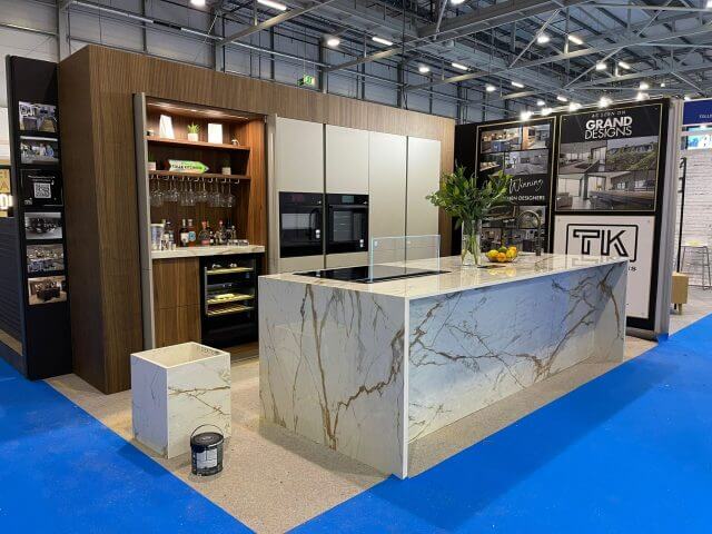 Tolle Kitchens Grand Designs show display with marble-effect island, walnut cabinetry and integrated wine cooler