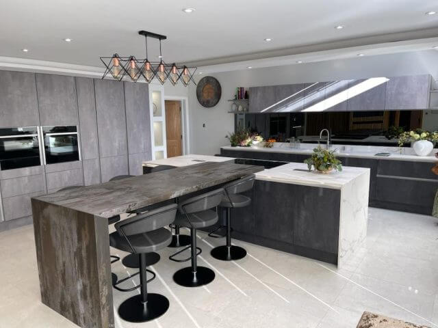 Large bespoke kitchen with concrete-effect units, stone breakfast bar and geometric pendant lighting by Tolle Kitchens