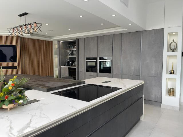Grey contemporary kitchen with white marble-effect quartz island worktop and integrated hob by Tolle Kitchens