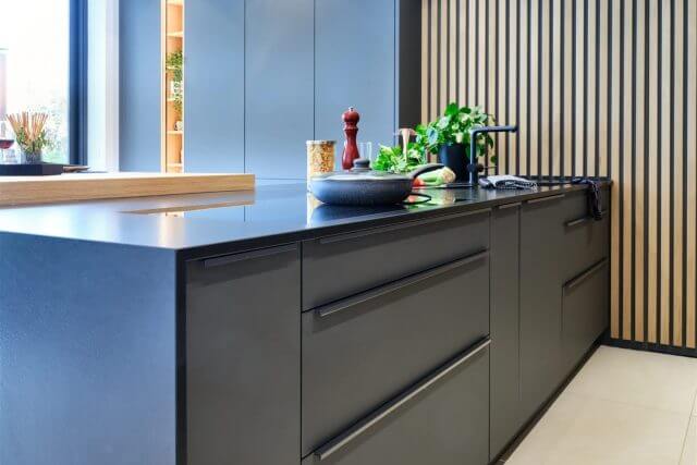 Close-up of handleless grey kitchen cabinetry with black worktop and wood slat wall
